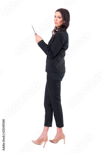 Side view of young elegant business woman holding tablet and looking at camera. Full body isolated on white background.