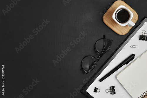 Mock up workspace with blank clip board, office supplies, pen, coffee cup, notepad and eyeglasses on dark background. Flat lay, top view, copy space