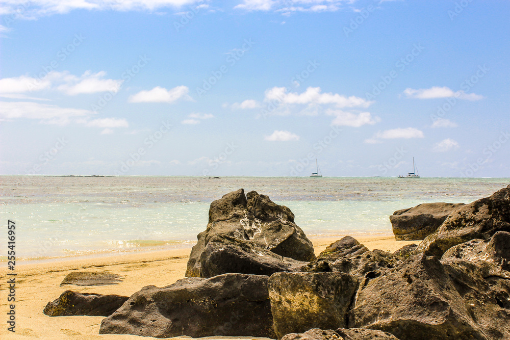 Volcanic Rocks on the beach in the Indian Ocean, Mauritius, golden sand and boats, para gliding out on the waves.
