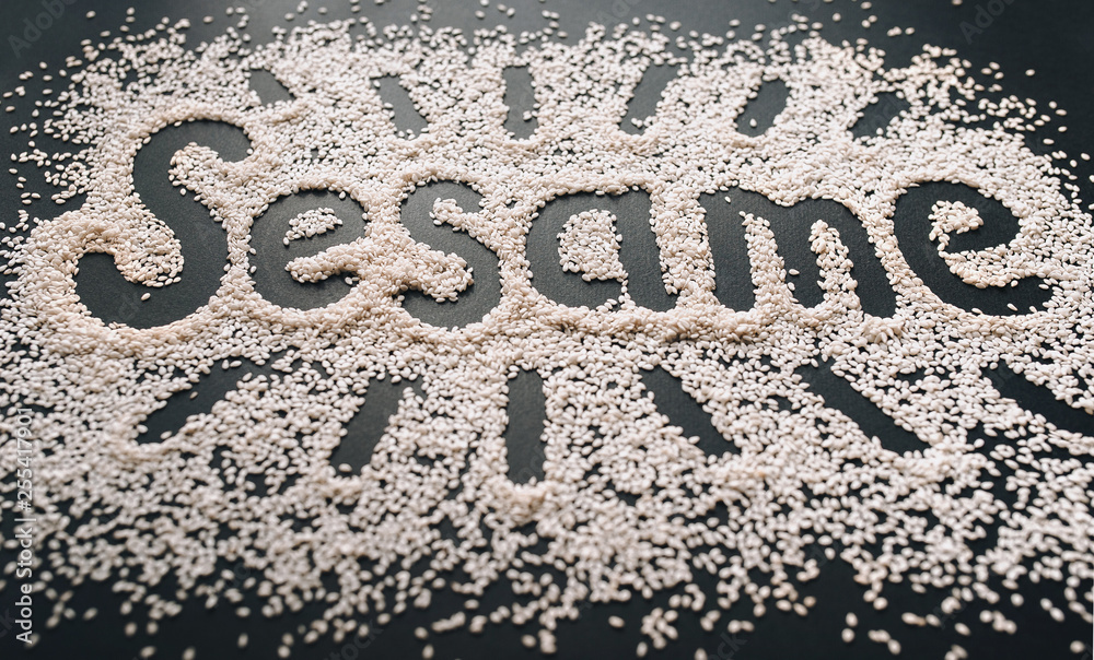 The funny big word Sesame is written among a multitude of grains on a black background. Symbol of healthy nutrition and vegetarianism. The funny big word Sesame is written among a multitude of grains on a black background. Symbol of healthy nutrition and vegetarianism.