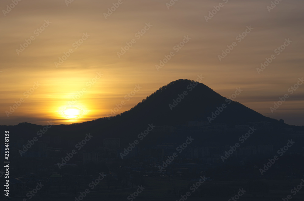 Scenic sunset landscape with golden sunlight above silhouette of mountains and clouds at the sky.