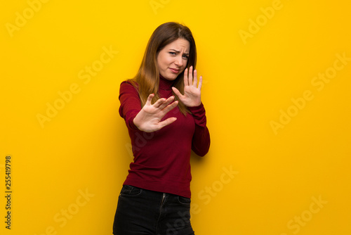 Woman with turtleneck over yellow wall nervous and scared stretching hands to the front