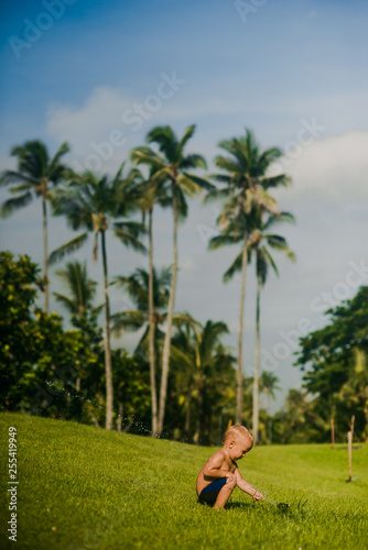 small baby playing in aweome park on background of tropical palms and blue sky in Bali