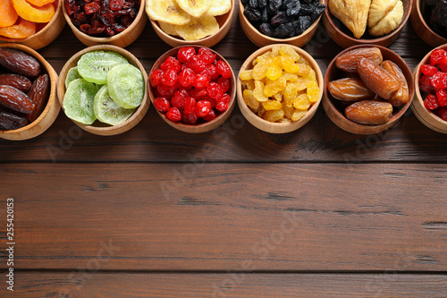Bowls of different dried fruits on wooden background, top view with space for text. Healthy lifestyle