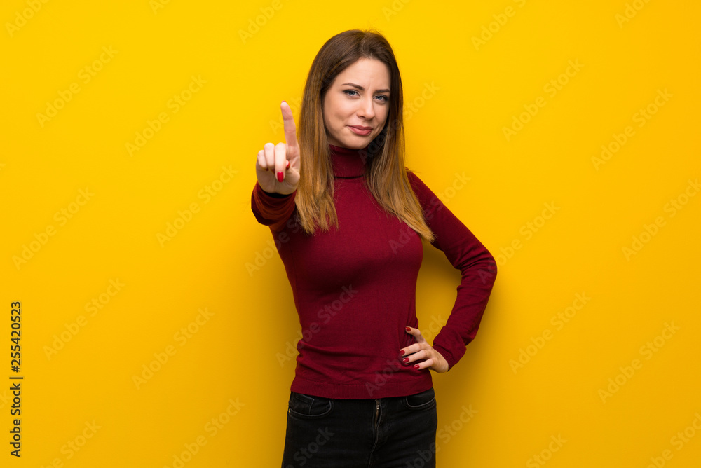 Woman with turtleneck over yellow wall showing and lifting a finger Woman with turtleneck over yellow wall showing and lifting a finger