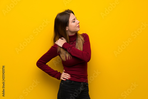 Woman with turtleneck over yellow wall suffering from pain in shoulder for having made an effort