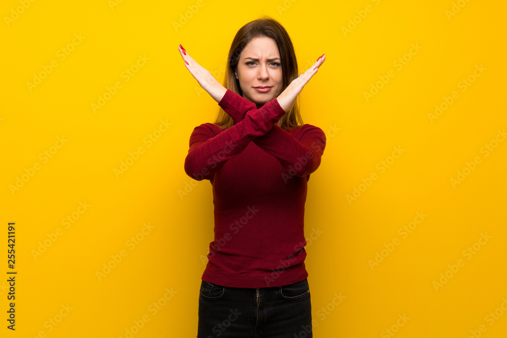 Woman with turtleneck over yellow wall making NO gesture Woman with turtleneck over yellow wall making NO gesture