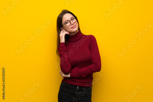Woman with turtleneck over yellow wall with glasses and smiling