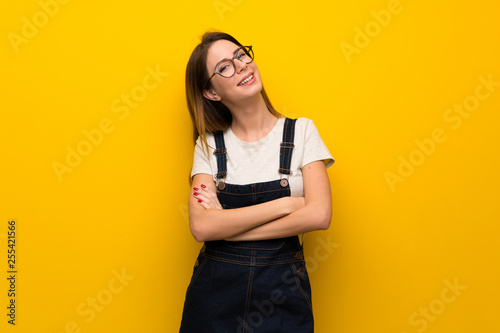 Woman over yellow wall looking up while smiling