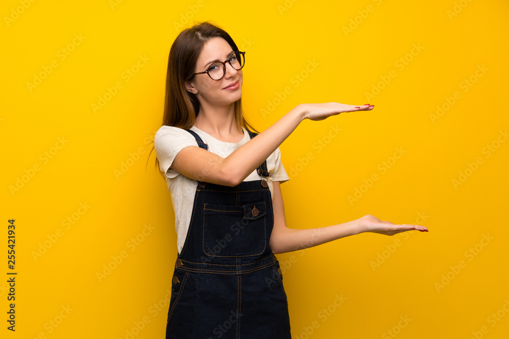 Woman over yellow wall holding copyspace to insert an ad Woman over yellow wall holding copyspace to insert an ad
