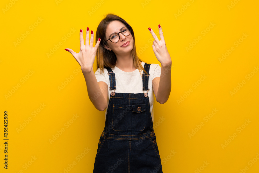 Woman over yellow wall counting seven with fingers Woman over yellow wall counting seven with fingers