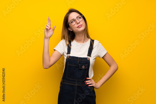 Woman over yellow wall with fingers crossing and wishing the best