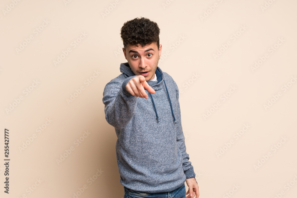 Young man over isolated wall surprised and pointing front