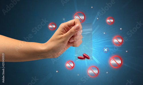 Hand giving pills with anti-drug concept and not allowed signs around photo