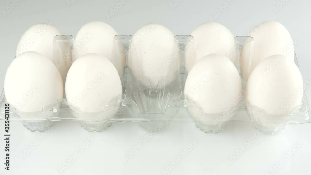 Large white chicken eggs in a transparent plastic tray on a white background. Female hands take eggs from the tray Large white chicken eggs in a transparent plastic tray on a white background. Female hands take eggs from the tray