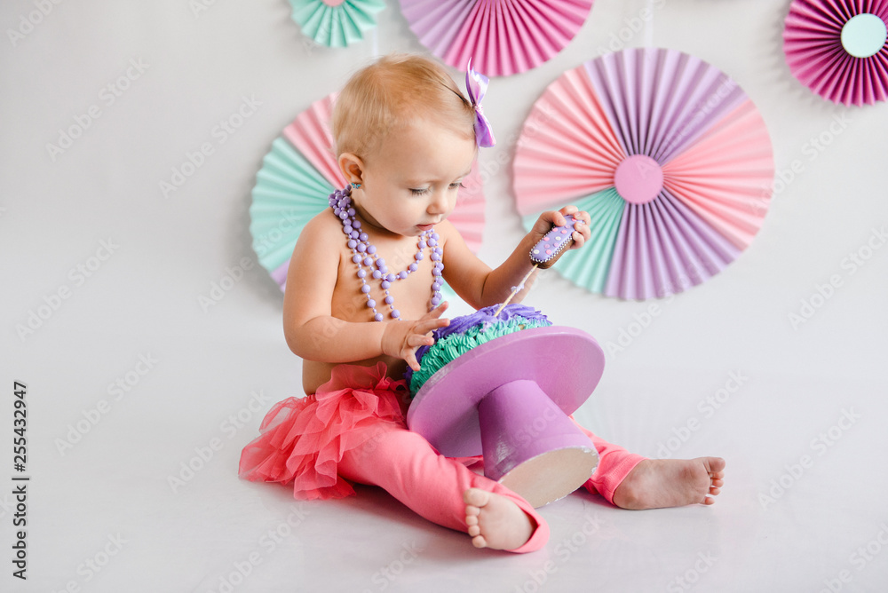 Fototapeta premium The little birthday girl was smeared into a cake. The use of the first cake. Smash cake. holiday decor photo shoot crush cake