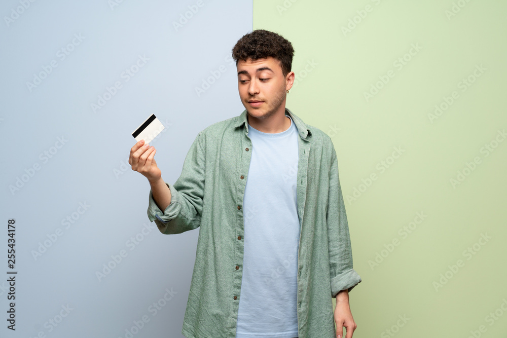 Young man over blue and green background taking a credit card without money Young man over blue and green background taking a credit card without money