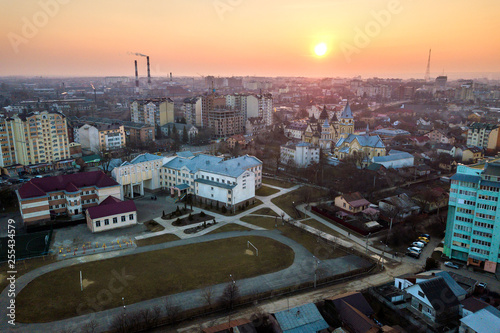 Top aerial view of urban city landscape. Apartment buildings, school, football field, church and houses on pink sky at sunrise background.