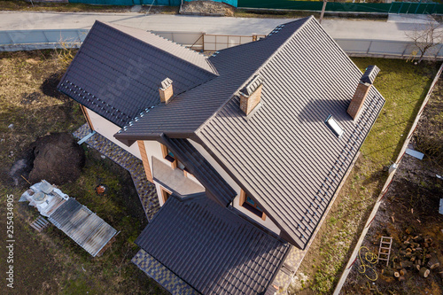 Aerial top view of building steep shingle roof, brick chimneys and small attic window on house top with metal tile roof. Roofing, repair and renovation work.