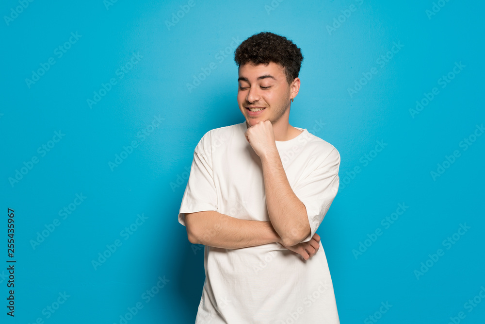 Young man over blue background looking down with the hand on the chin