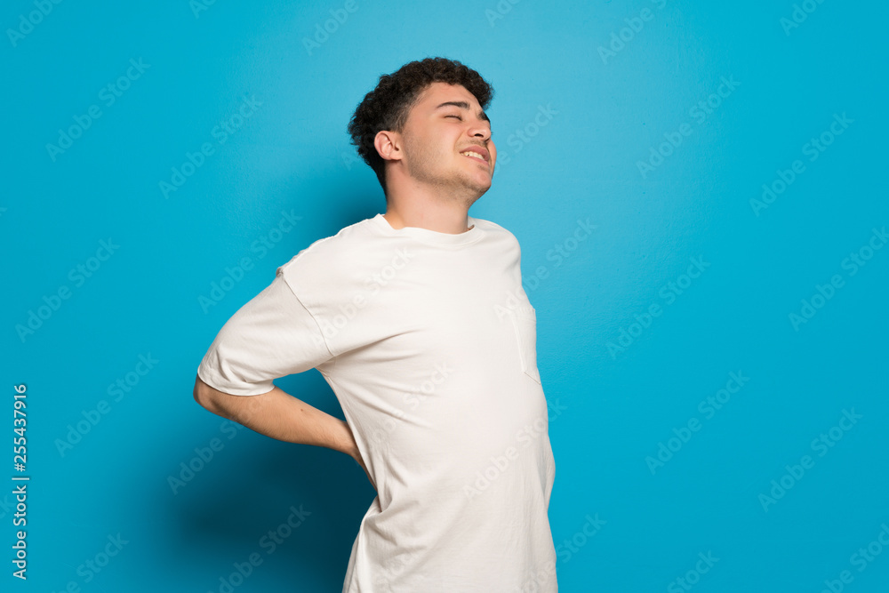 Young man over blue background suffering from backache for having made an effort Young man over blue background suffering from backache for having made an effort