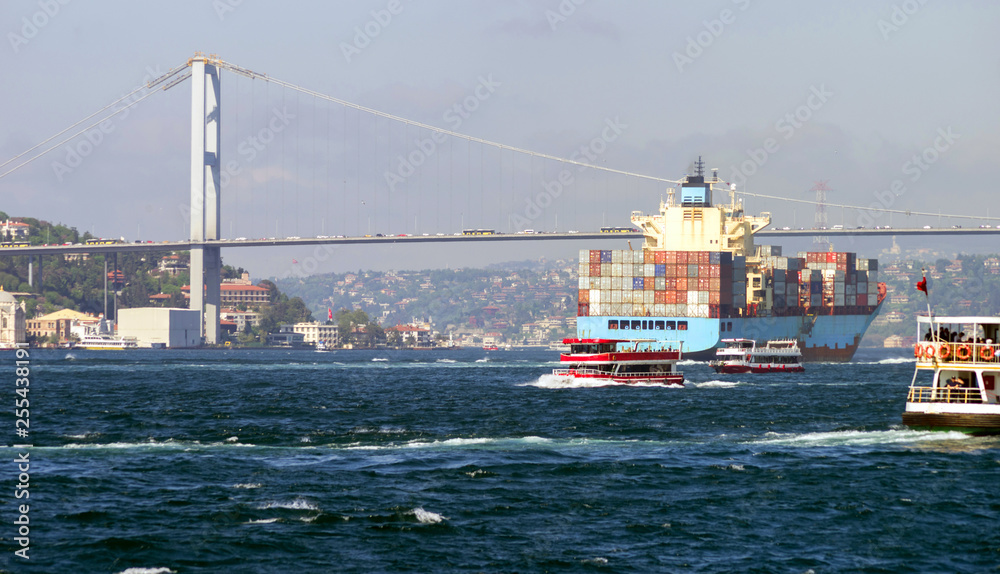 A container ship and several small passenger ships near the 15 July Martyrs Bridge on the Bosphorus. Istanbul, Turkey. Selective focus.