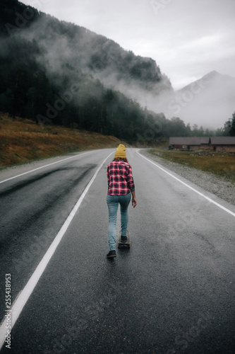 fashionable hipster girl rides a skateboard on the road in the mountains around the mountain and beautiful view