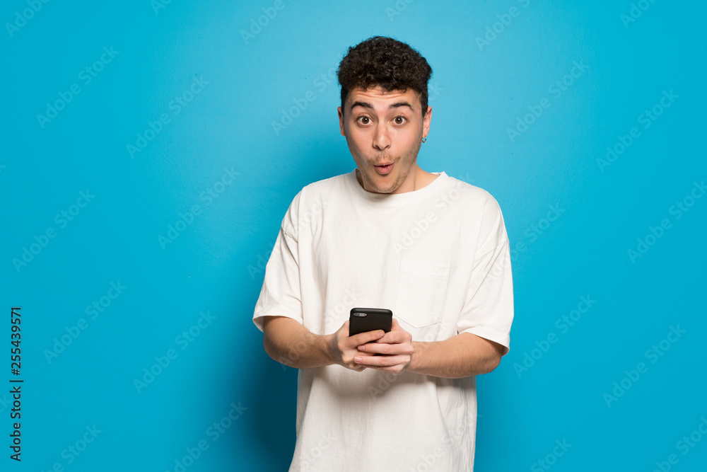 Young man over blue background surprised and sending a message Young man over blue background surprised and sending a message