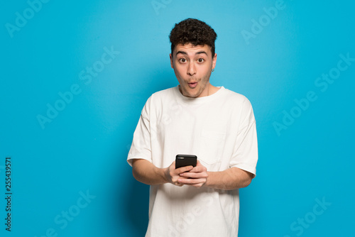 Young man over blue background surprised and sending a message © luismolinero