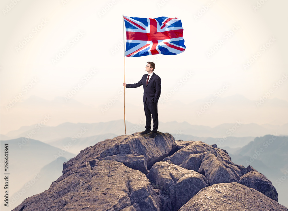 Obraz premium Successful businessman on the top of a mountain holding victory flag 