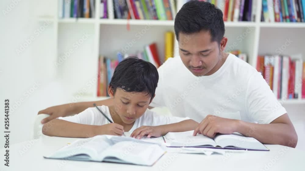 Little boy doing homework while writing on a book with his father at home. Shot in 4k resolution Little boy doing homework while writing on a book with his father at home. Shot in 4k resolution