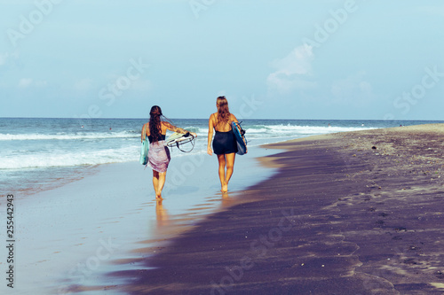 Photography Two surfing girls walking on the beach with surfing boards