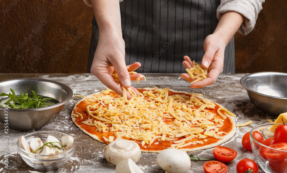 Chef adding cheese to pizza at kitchen