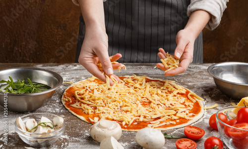 Chef adding cheese to pizza at kitchen
