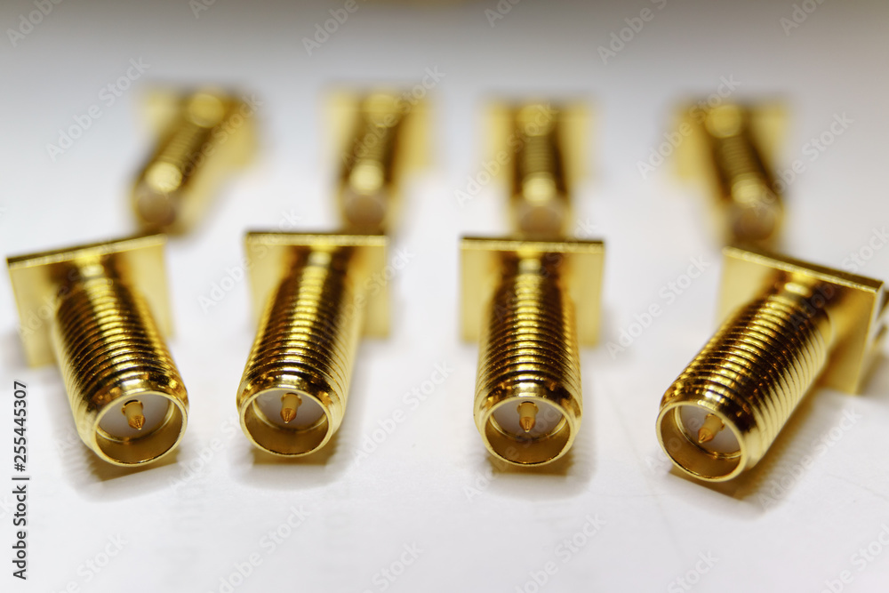 Close-up of scattered gold plated SMA male connectors electronics components in partial focus on white background Close-up of scattered gold plated SMA male connectors electronics components in partial focus on white background