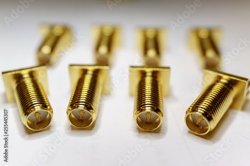 Close-up of scattered gold plated SMA male connectors electronics components in partial focus on white background