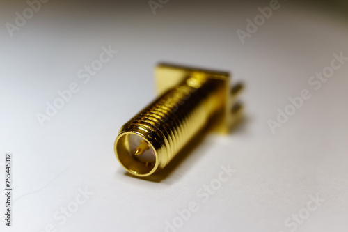 Close-up of gold plated SMA male connector electronics component in partial focus on white background