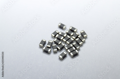 Abstract close-up of grey scattered 0402 SMT surface mount chip ferrite bead power electronics components on white background in random pattern