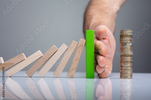 Person Stopping Dominos From Falling With Stacked Coins