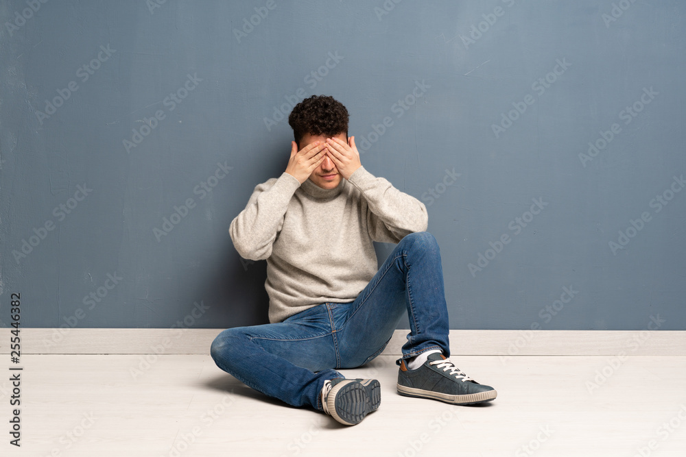 Young man sitting on the floor covering eyes by hands Young man sitting on the floor covering eyes by hands