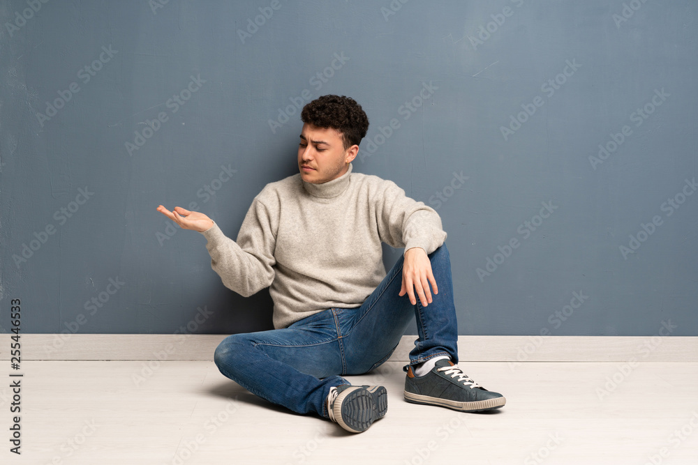 Young man sitting on the floor holding copyspace with doubts Young man sitting on the floor holding copyspace with doubts
