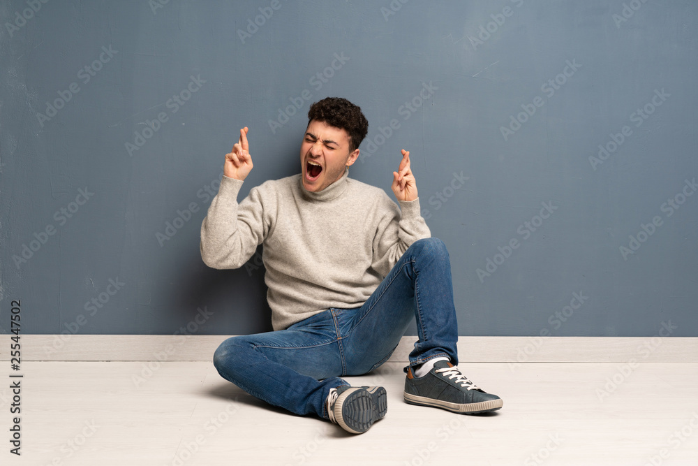Young man sitting on the floor with fingers crossing Young man sitting on the floor with fingers crossing