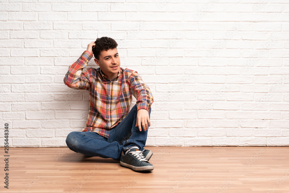 Young man sitting on the floor having doubts while scratching head Young man sitting on the floor having doubts while scratching head