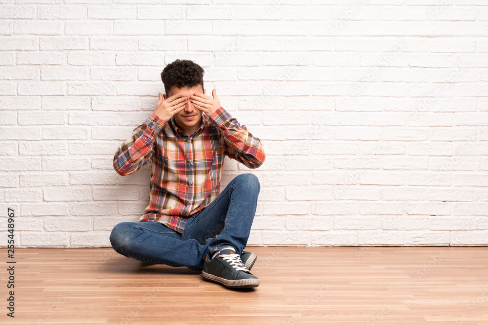 Young man sitting on the floor covering eyes by hands Young man sitting on the floor covering eyes by hands
