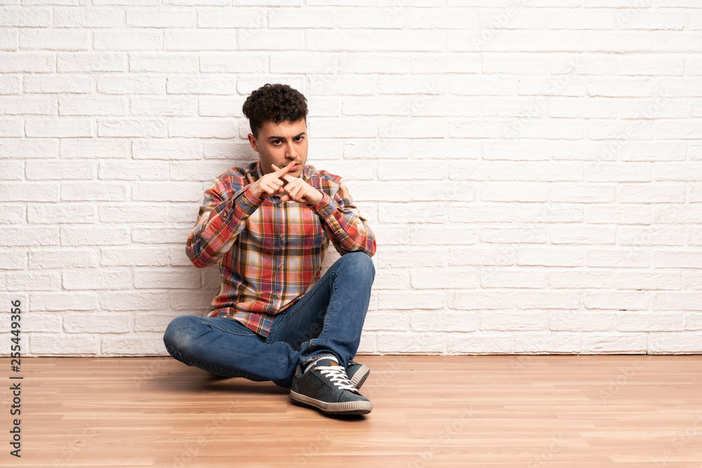 Young man sitting on the floor showing a sign of silence gesture Young man sitting on the floor showing a sign of silence gesture