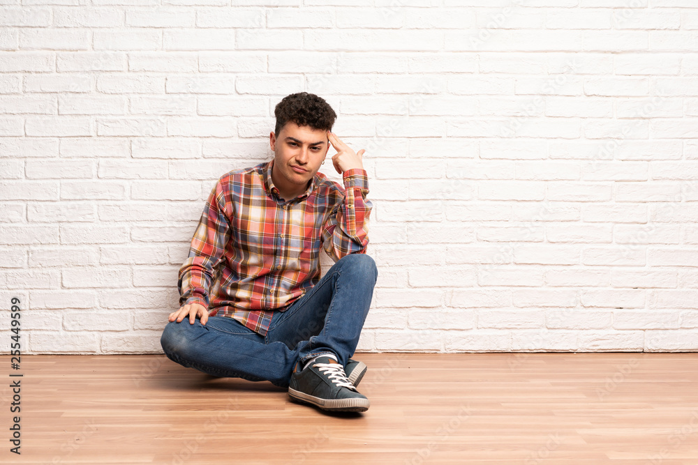 Young man sitting on the floor with problems making suicide gesture Young man sitting on the floor with problems making suicide gesture