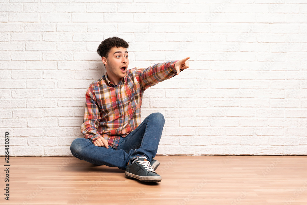 Young man sitting on the floor pointing away Young man sitting on the floor pointing away