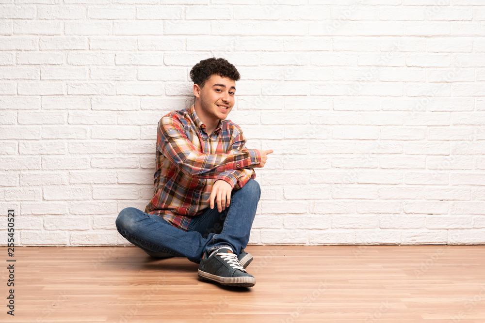 Young man sitting on the floor pointing back Young man sitting on the floor pointing back