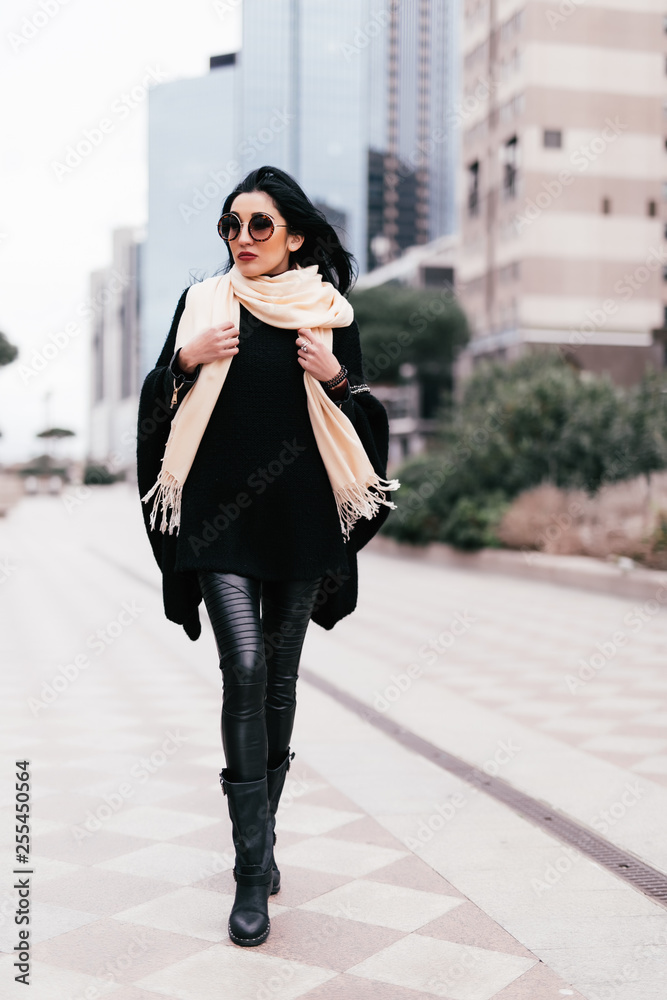 Fototapeta premium Outdoors fashion portrait of stunning trendy woman posing on the street. Smiling and walking on the city. Going shopping. Wearing stylish white fitted coat, round rim sunglasses. Waiting for. Close up