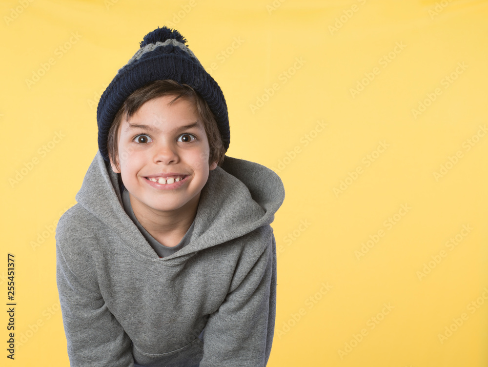 Smiling, school age boy in gray sweatshirt and ski hat isolated on yellow background Smiling, school age boy in gray sweatshirt and ski hat isolated on yellow background